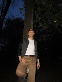 Portrait of young man standing by tree trunk at night