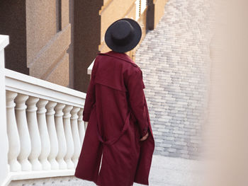 Back view woman walking on city street at sunset wearing hat and coat