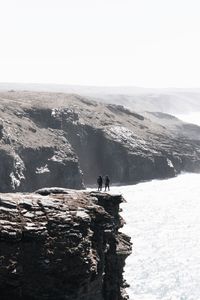 Men standing on cliff against sky during winter