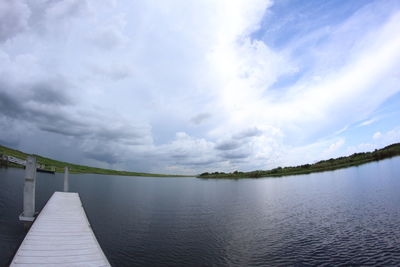 Fish-eye view of jetty in river against cloudy sky