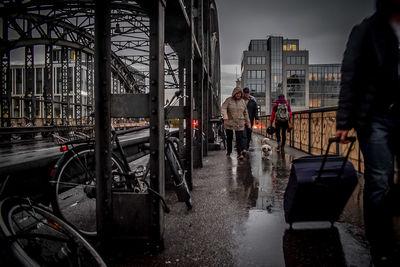 Rear view of people walking on wet road in city during rainy season