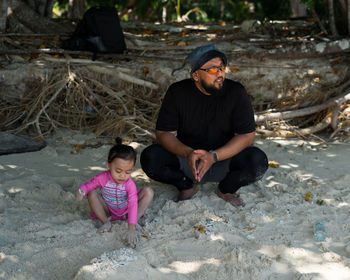 Full length of father and daughter crouching on sand at beach