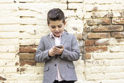 Boy using mobile phone while standing against brick wall