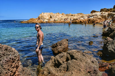 Man standing on rock by sea against sky