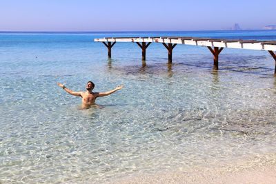 Full length of shirtless man in sea against sky