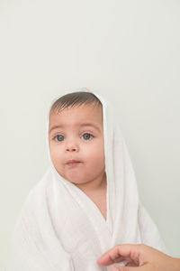 Thoughtful cute baby boy wrapped in towel while sitting against wall