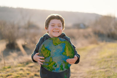 Portrait of cute boy holding globe against sky
