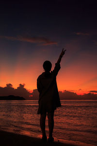 Rear view of silhouette man standing at beach during sunset