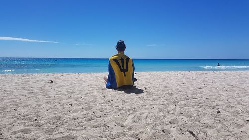 Rear view of man sitting on beach against sky 