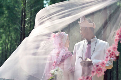 Smiling bride and groom standing in forest seen through scarf