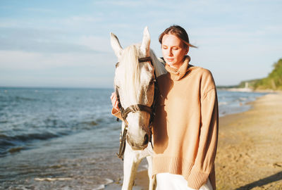 Young woman in beige sweater with white horse on seascape background