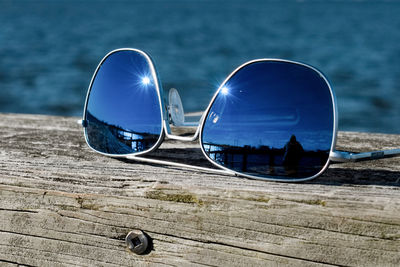 Reflective blue lens sunglasses on wooden rail with blue water in the background