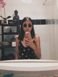 Woman photographing with mobile phone while reflecting on mirror in bathroom