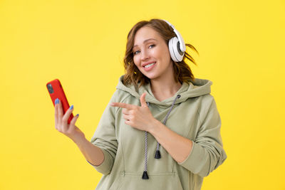 Smiling young woman using mobile phone against yellow background