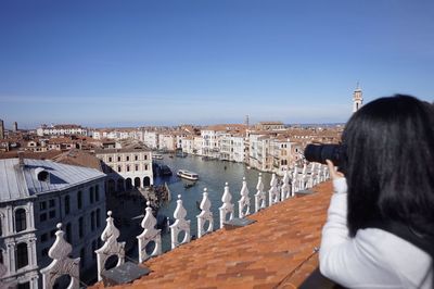 Rear view of woman looking at cityscape against clear sky