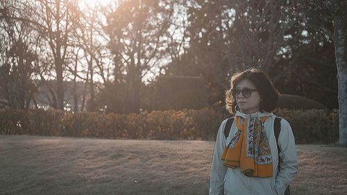 Young woman standing against trees during sunset