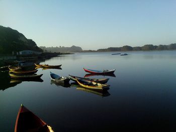 Boats moored on calm lake against clear sky