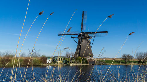 Traditional windmill by lake against blue sky