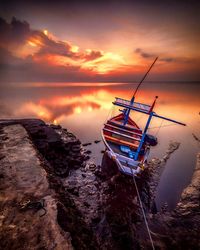 Boat moored on seashore against sky during sunrise