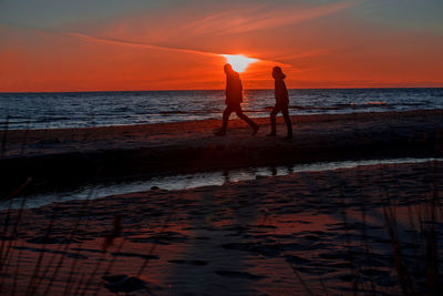 Silhouette friends walking on shore at beach during sunset