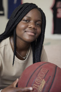 Portrait of smiling female teenager holding basketball while sitting at home