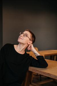 Young woman with short hair in eyeglasses and black sweater sitting at the table in office