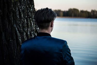 Rear view of man standing by tree trunk in lake