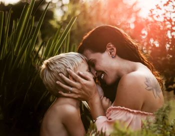 Side view of mother embracing son by plant