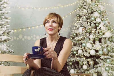 Woman in the new year at the ice rink drinks coffee sitting on a bench next to the christmas tree