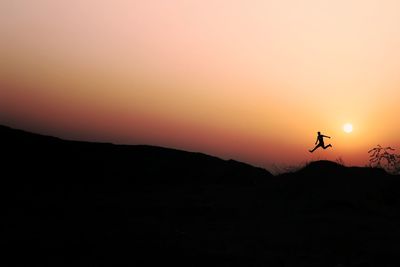 Silhouette of birds flying over land against orange sky