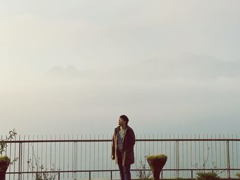 Man standing by railing against cloudy sky