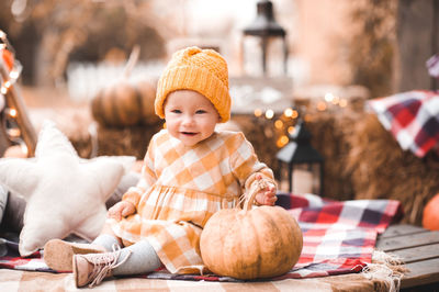 Smiling baby girl 1-2 year old wearing yellow stylish dress and knitted hat posing over autumn