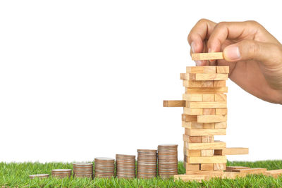 Cropped hand playing block removal game with stacked coins on grass against white background