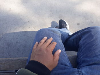 Low section of man sitting on bench over footpath