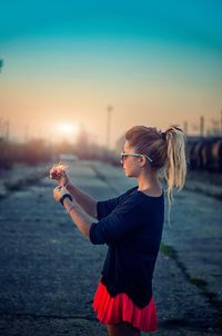 Side view of woman standing on land against sky during sunset