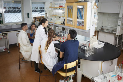 Mature teacher explaining to young multi-ethnic university students sitting in chemistry laboratory