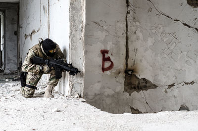 Full length of army soldier with gun by graffiti on wall