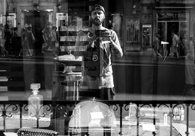 Young man reflecting on glass window while photographing outside store