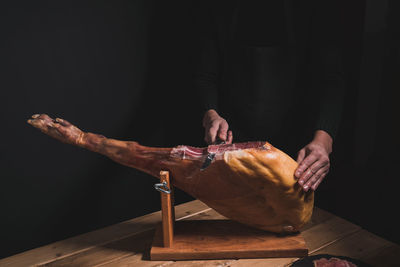 Chef cutting ham with a knife on a wooden table on a black background