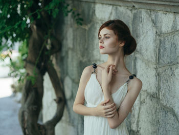 Young woman looking away while standing against wall