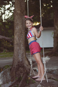 Full length portrait of smiling girl standing against tree