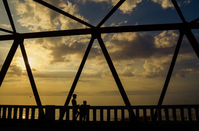 Silhouette bridge over sea against sky during sunset