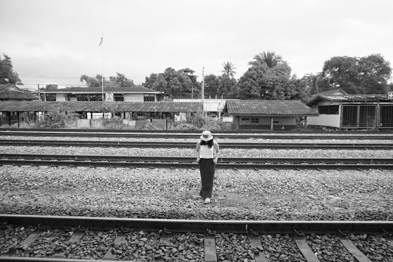 railroad track, rail transportation, full length, architecture, built structure, tree, lifestyles, building exterior, railing, public transportation, railroad station platform, rear view, casual clothing, railroad station, walking, transportation, standing, leisure activity