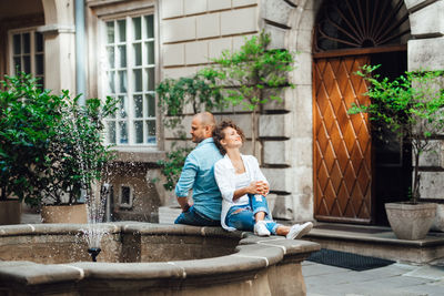 Woman sitting outside house against building