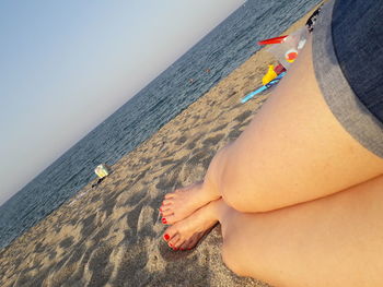 Low section of woman lying at beach against clear sky