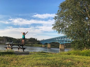 Man standing on bridge by tree against sky