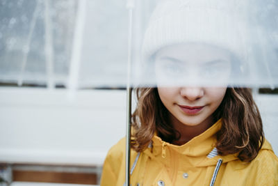 Girl wearing raincoat hiding face under umbrella outdoors