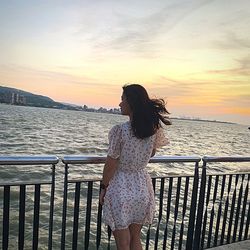 Rear view of woman looking at sea against sky during sunset