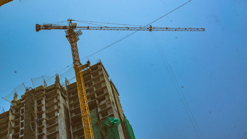 Low angle view of crane by building against clear blue sky