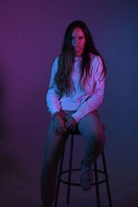 Portrait of teenage girl sitting over purple background